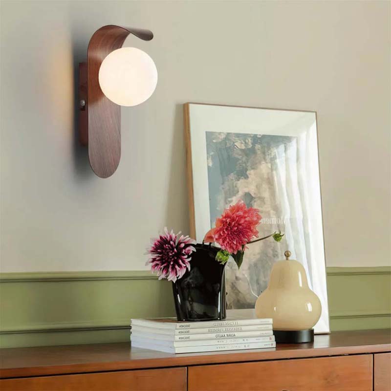 Wall sconce on a wall with a vase of flowers and books on a wooden surface.