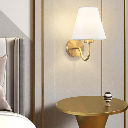 Gold wall sconce with white shade on a wall next to a round gold table.