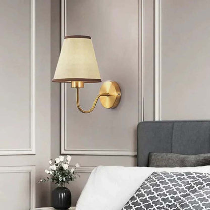 Wall-mounted lamp with a decorative shade on a wall above a bed.