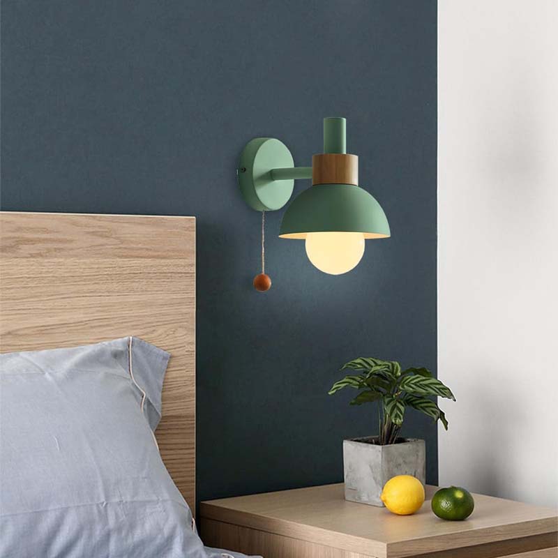 Green wall lamp on a dark blue wall above a bed with a wooden headboard.
