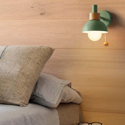Green wall lamp on a wooden wall above a bed with pillows.
