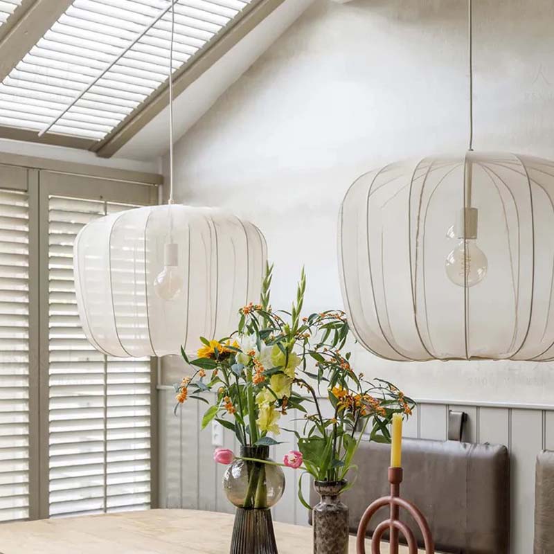 Two hanging pendant lights in a room with a vase of flowers and candles on a table.