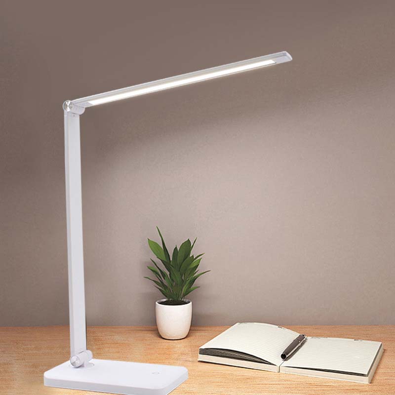 White LED desk lamp on a wooden surface with a plant and notebook.