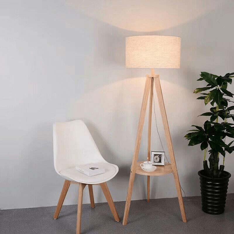 Wooden floor lamp with a white shade next to a chair and plant in a room.