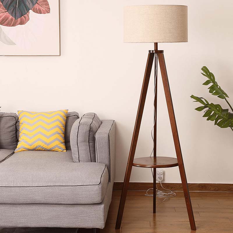 Wooden tripod floor lamp next to a gray sofa with a yellow pillow in a living room setting.