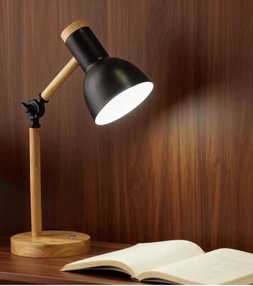 Black Adjustable Nordic Wood Desk Lamp sits on a desk, illuminating a book against a dark backdrop.