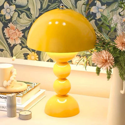 Yellow table lamp on a desk with decorative items and floral wallpaper.