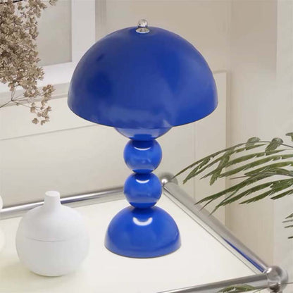 Blue table lamp on a glass table with a white vase and plant in the background