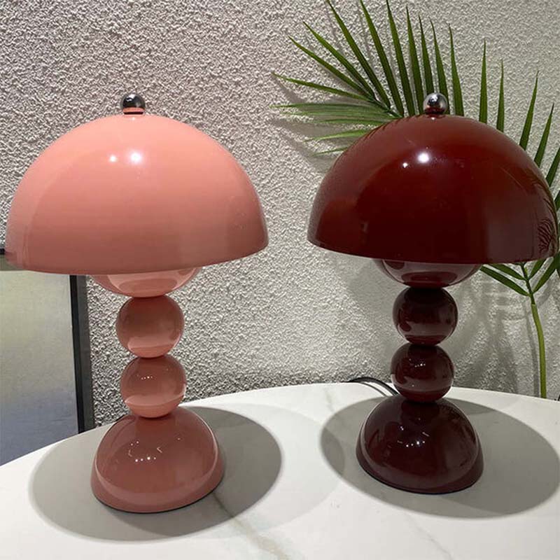 Two table lamps, one pink and one red, on a white surface with a plant in the background.