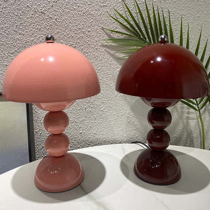 Two table lamps, one pink and one red, on a white surface with a plant in the background.