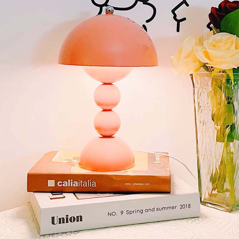 Pink table lamp on books with a vase of flowers in the background