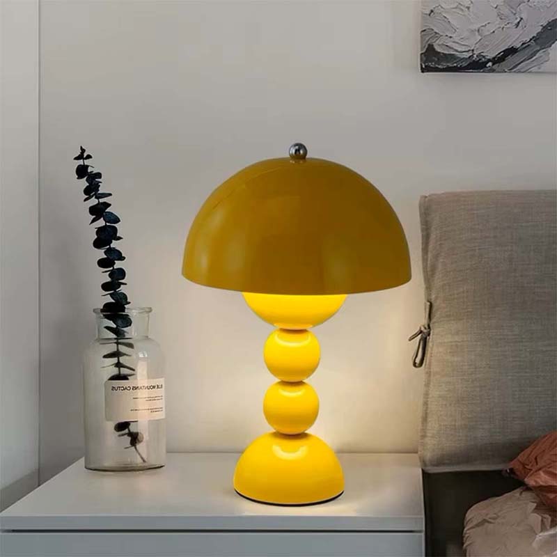 Yellow table lamp on a nightstand with a vase and plant in the background.