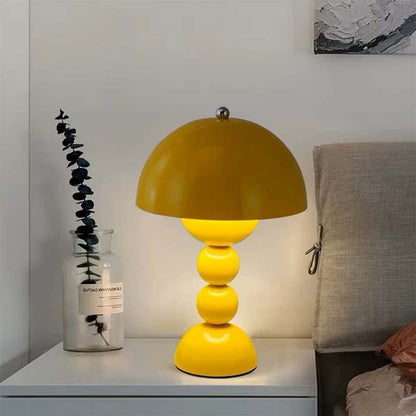 Yellow table lamp on a nightstand with a vase and plant in the background.