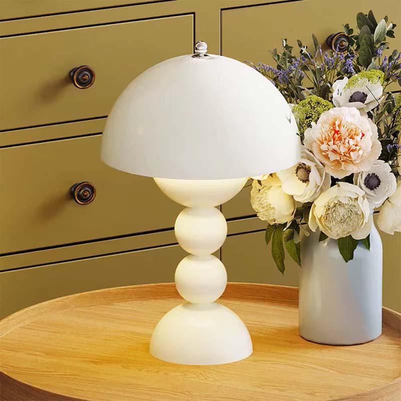 White table lamp on a wooden surface with a vase of flowers in the background.