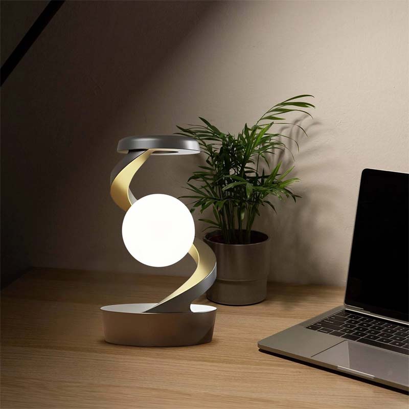 Saturn Helix – LED Desk Lamp with Wireless Charging on a wooden surface with a laptop and a plant in the background.
