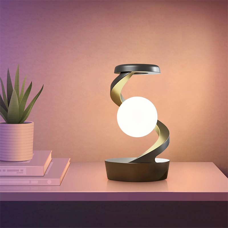 Saturn Helix – LED Desk Lamp with Wireless Charging on a table next to a plant and books.