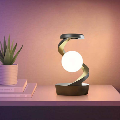Saturn Helix – LED Desk Lamp with Wireless Charging on a table next to a plant and books.