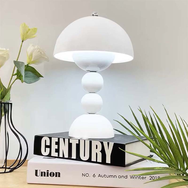 White table lamp on books with a vase of flowers and plant in the background