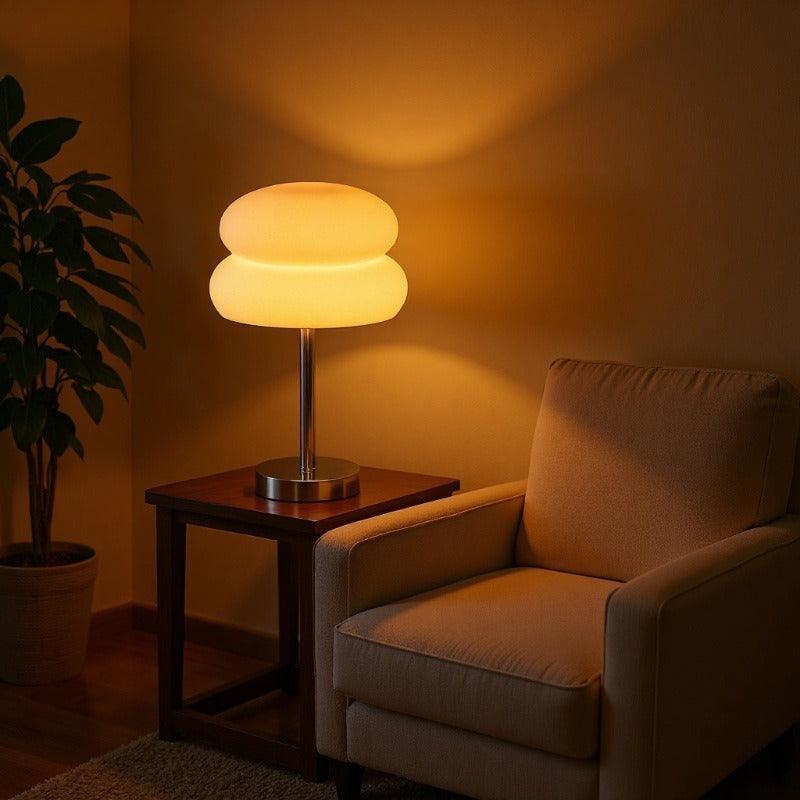 Retro Sandwich Glass Table Lamp placed on a dark wood side table next to a beige armchair in a warmly lit room.