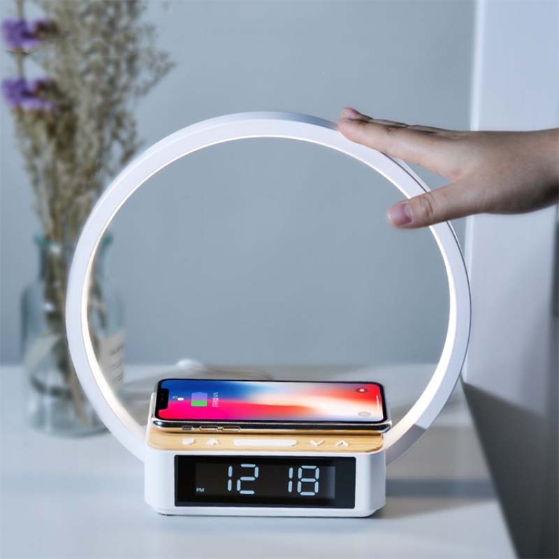 Round digital clock with wireless charging pad on a surface, hand holding it.