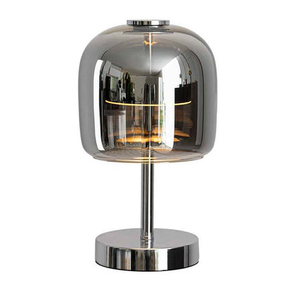 A modern table lamp with a rounded, dome-shaped smoked glass shade, a polished chrome metal stem, and a circular chrome base, shown on a plain white background.