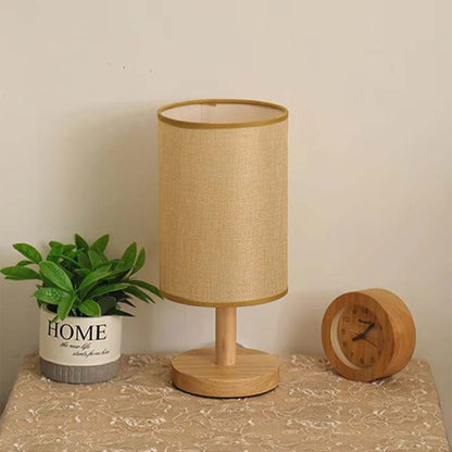 Wood Table Lamp with Natural Fabric Shade on a table between a flower and a clock