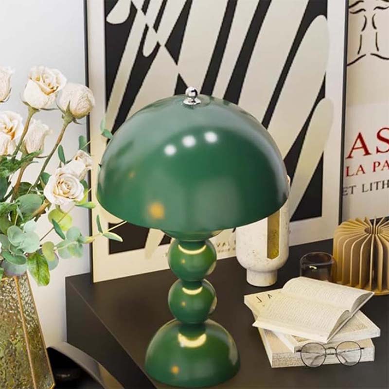 Green table lamp on a desk with decorative items and flowers.