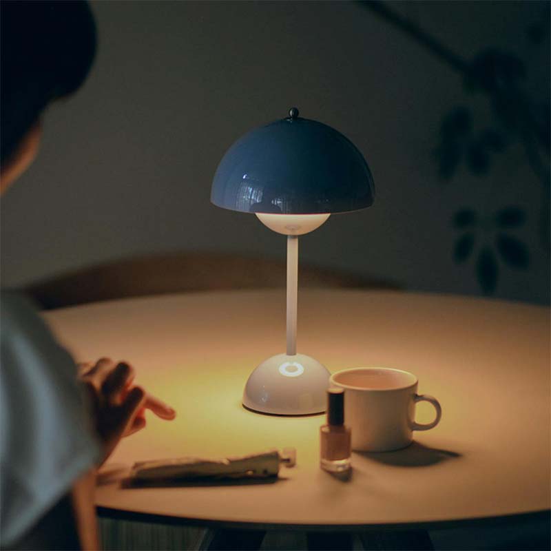 Person pointing at a blue lamp on a table with a cup and other items.