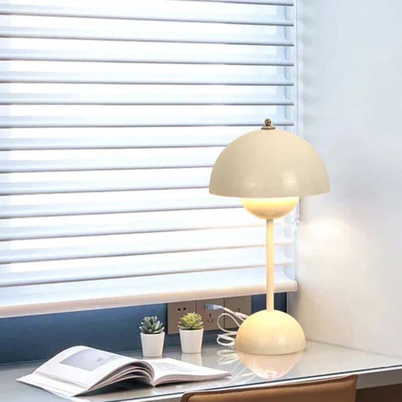 Beige table lamp on a desk with a window and power outlet in the background