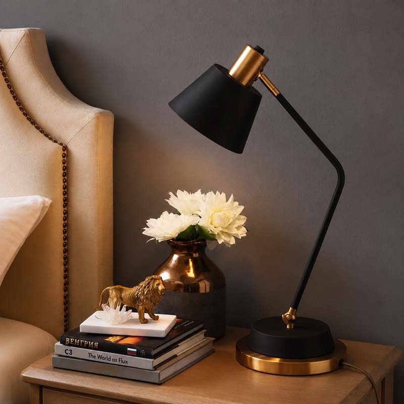 A black Modern Adjustable LED Reading Desk Lamp sits on a wooden nightstand next to a beige upholstered chair and white flowers in a metal vase.