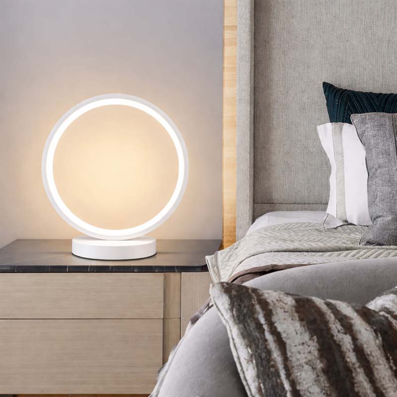 Modern ring lamp on a bedside table next to a bed in a cozy bedroom.