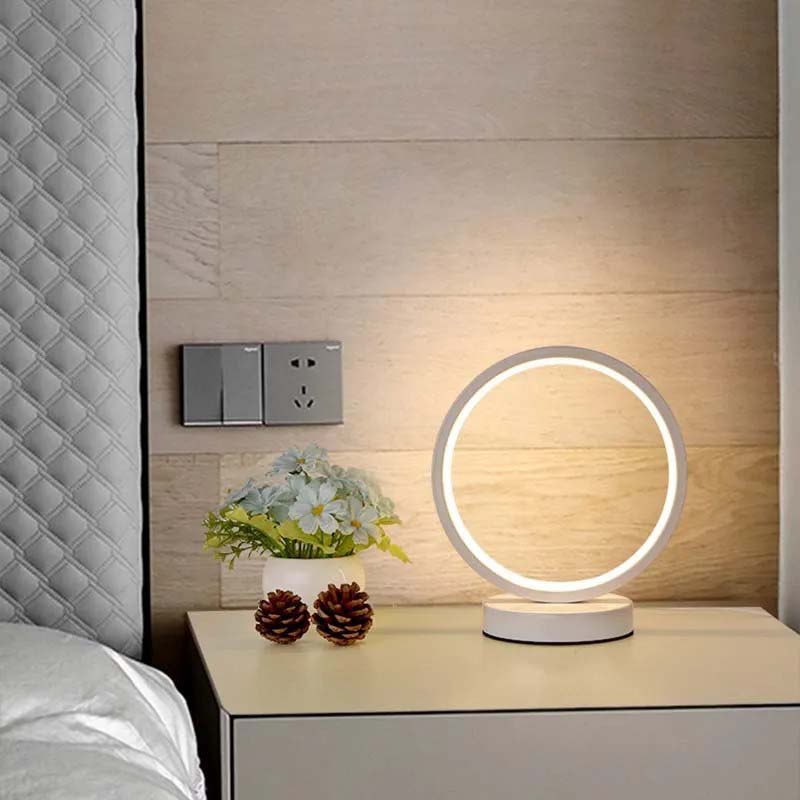 LED ring bedside lamp with soft lighting on a nightstand, next to flowers and decor.