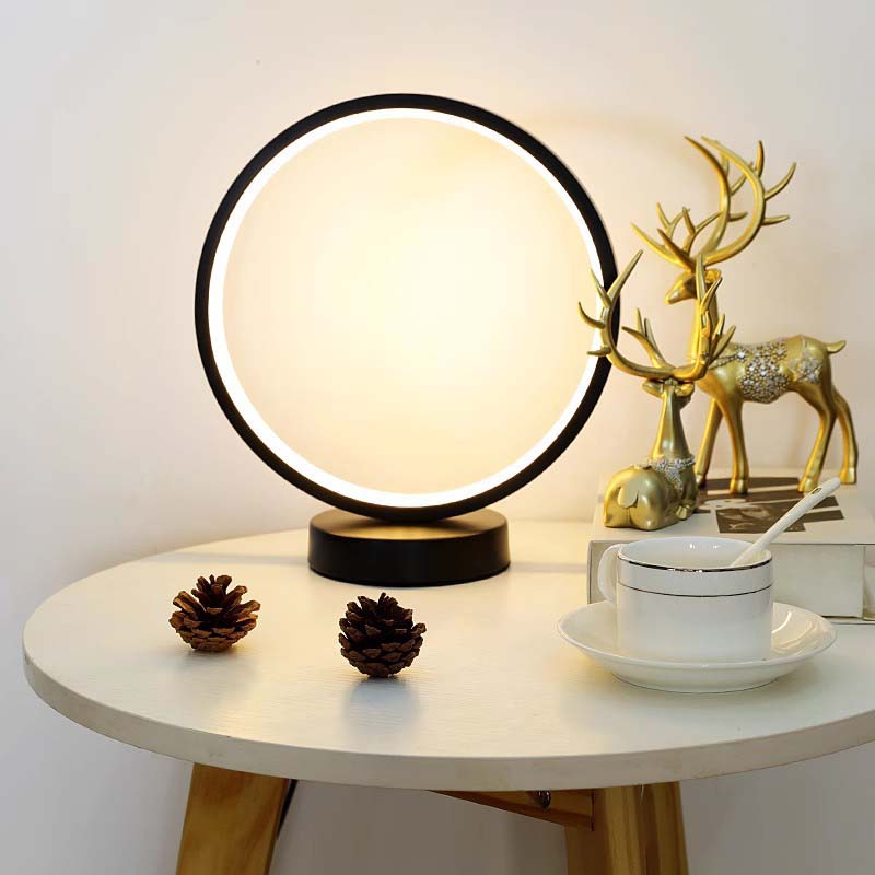 Modern ring lamp with warm LED light on a white side table, next to pine cones, a gold deer decor, and a cup