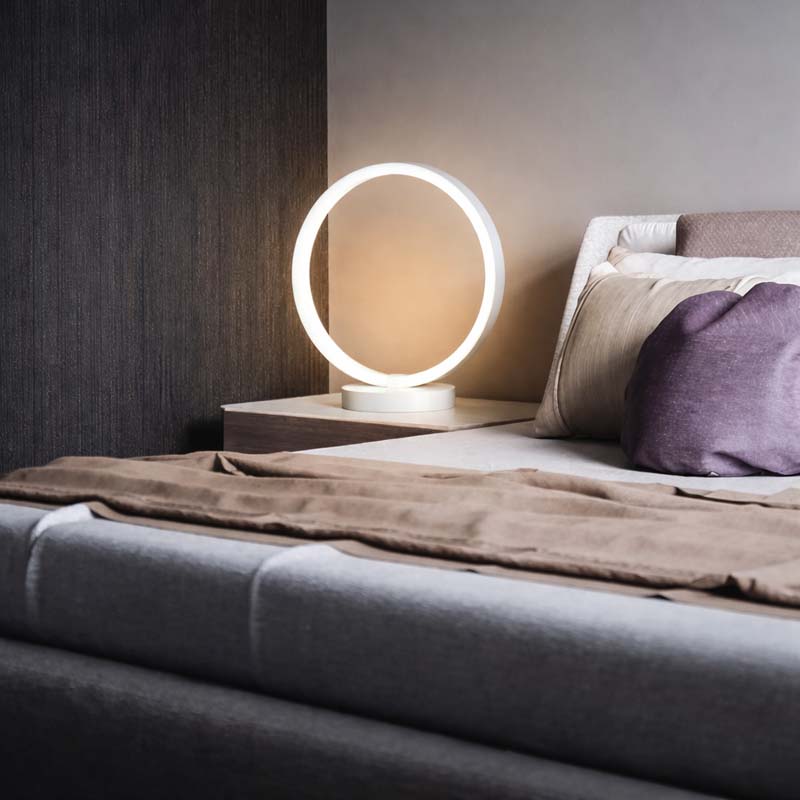 Modern LED ring table lamp on bedside table, minimalist bedroom lighting, warm ambient glow, contemporary home decor