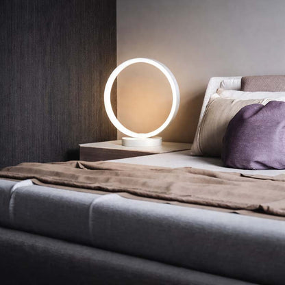 Modern LED ring table lamp on bedside table, minimalist bedroom lighting, warm ambient glow, contemporary home decor