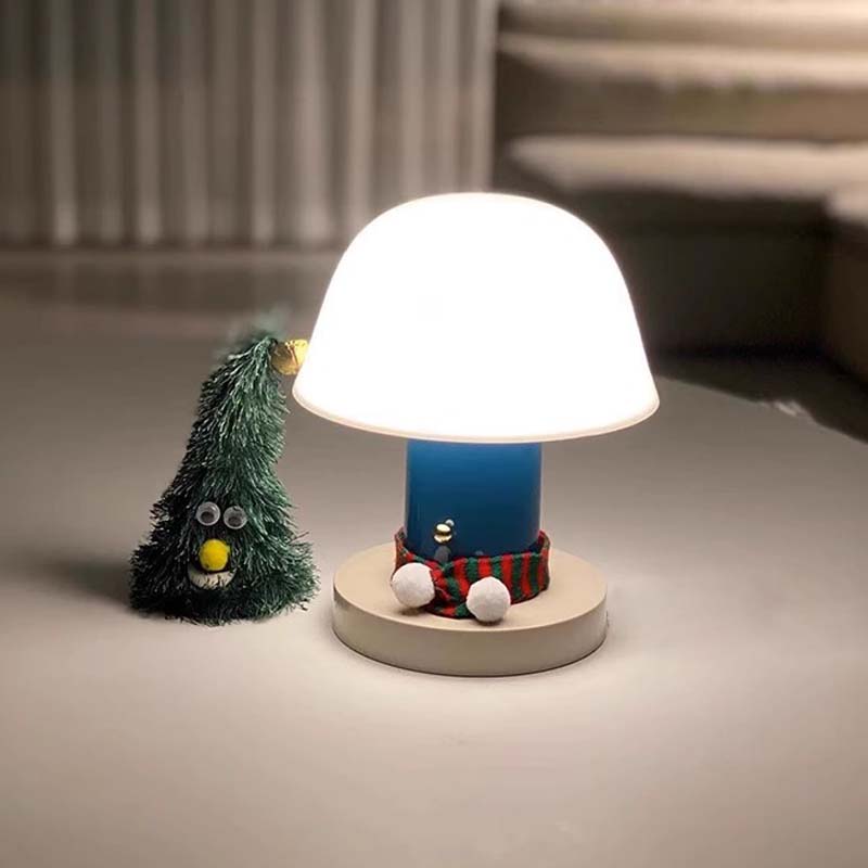 The Nordic Mushroom LED Table Lamp is pictured on the tabletop next to a small green fluffy Christmas tree decoration.