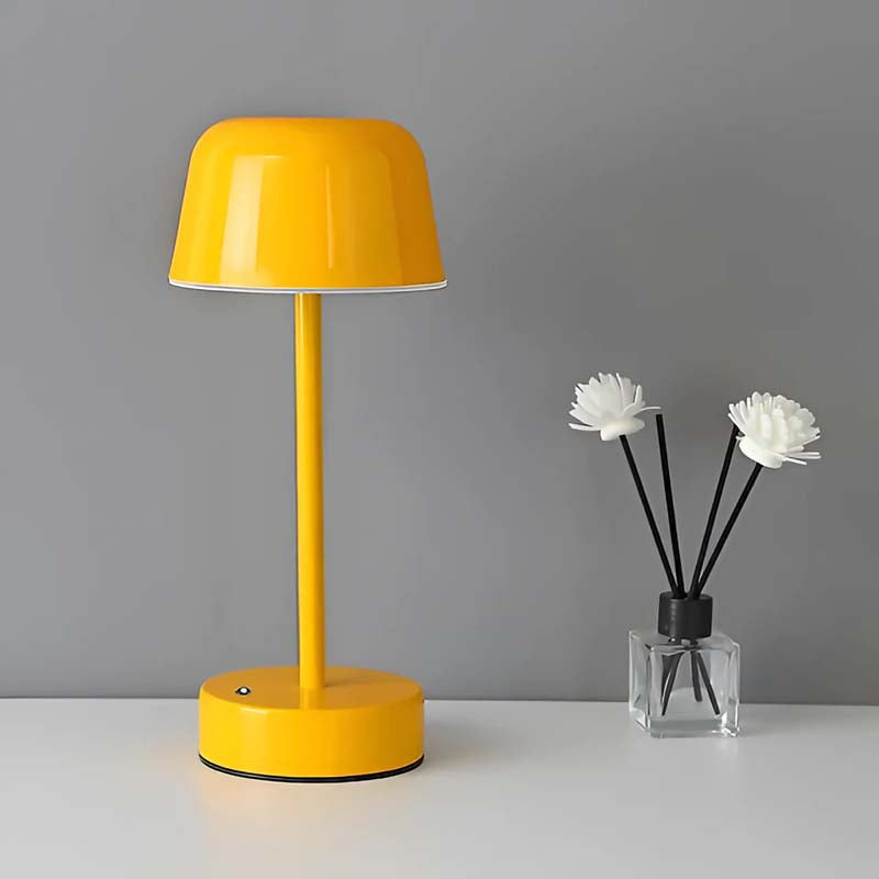 A yellow Rechargeable Cordless Touch LED Table Lamp sits on a white surface next to a glass vase with white flowers, against a solid gray background.