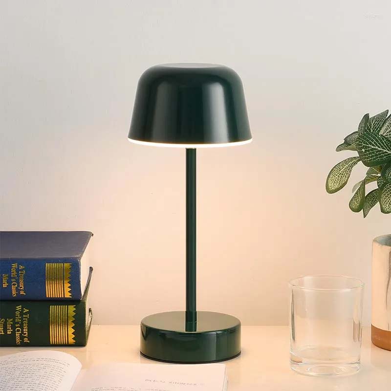 A black Rechargeable Cordless Touch LED Table Lamp sits on a table, with books and a plant in the background.