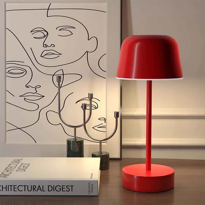 A red Rechargeable Cordless Touch LED Table Lamp sits on a wooden surface, with a book and abstract artwork in the background.