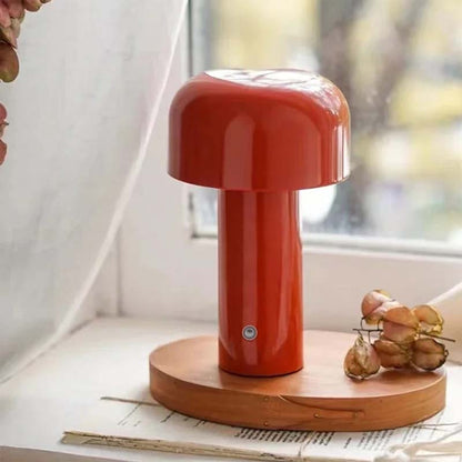 A glossy red Rechargeable Mushroom LED Table Lamp sits on a round wooden stand on a windowsill against a backdrop of dried flowers and a curtain.