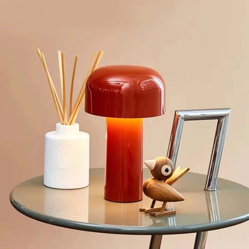 Red lamp, white vase with sticks, and wooden owl figurine on a glass table against a beige background