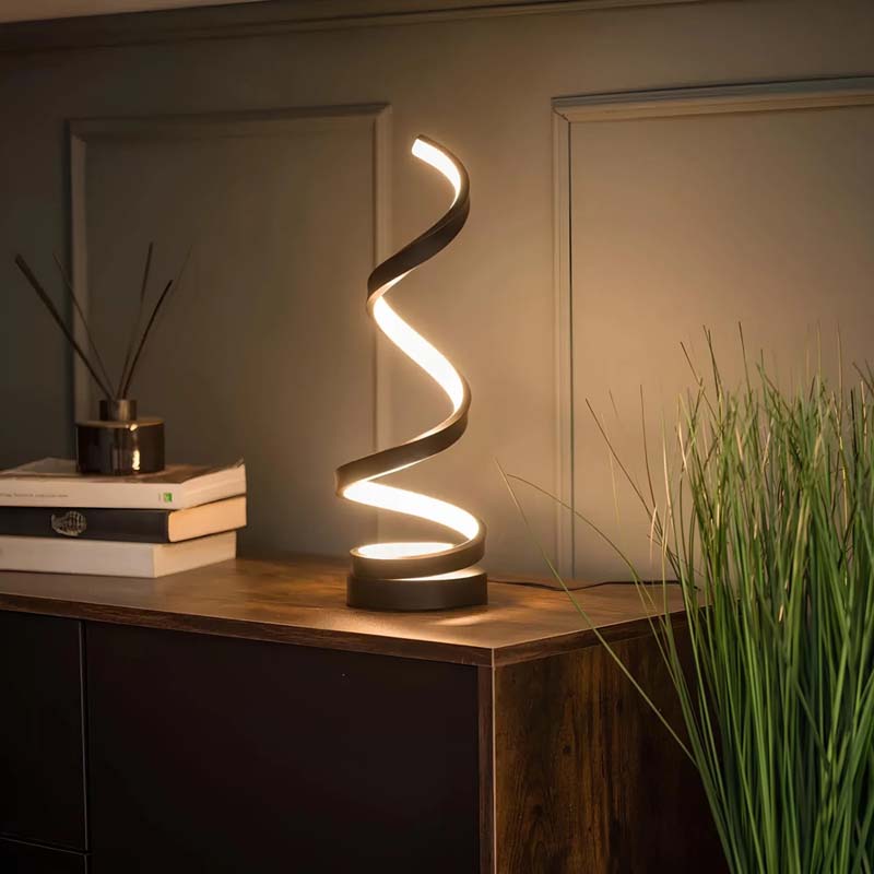 Spiral table lamp on a wooden surface with books and a plant in the background