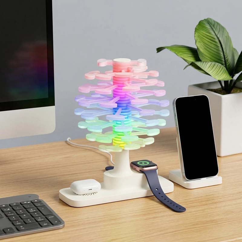 Spiral Tree LED Desk Lamp shown on a wooden desk with a smartphone, smartwatch, headphone case, next to a keyboard and a houseplant.