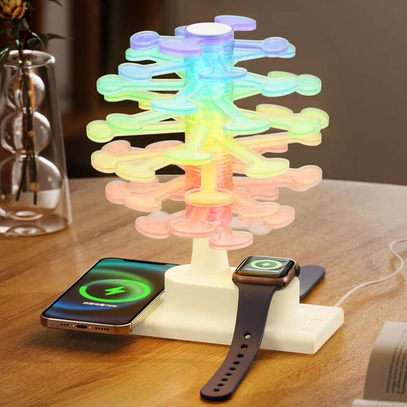 The Spiral Tree LED Desk Lamp, which charges a smartphone and smartwatch, is shown on a wooden table. The lamp shimmers with rainbow colors.