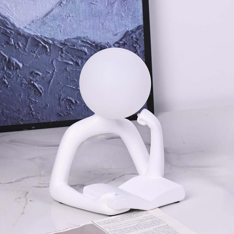 Thinker Statue LED Table Lamp stands on a light marble surface in front of a framed abstract print.