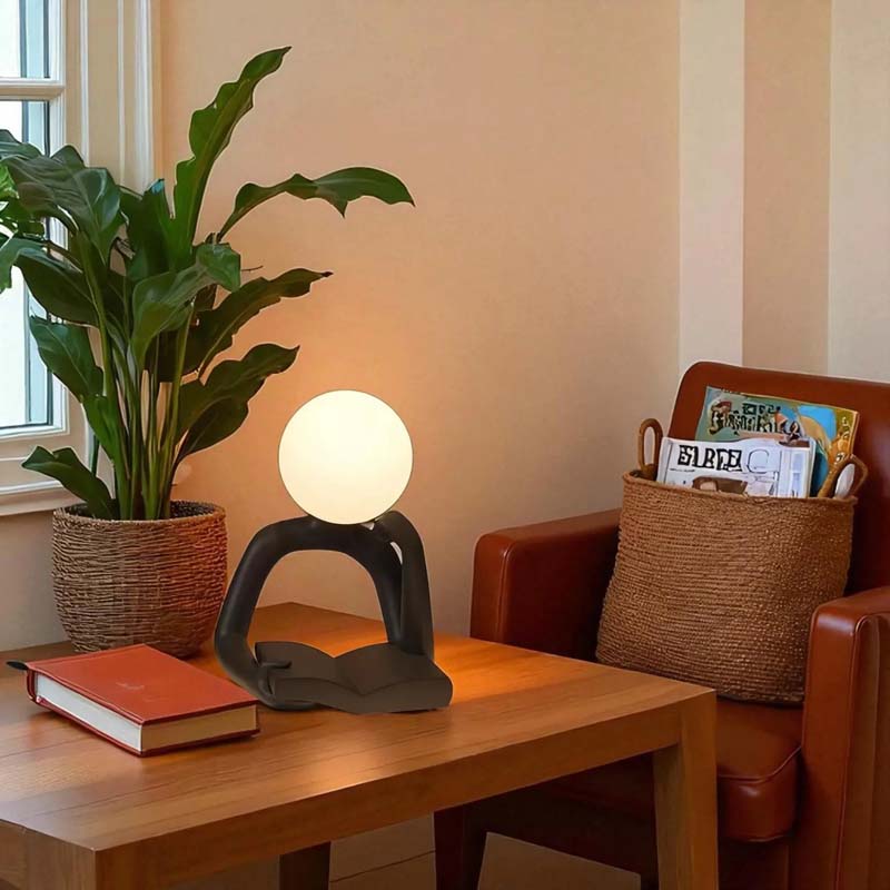 Thinker Statue LED Table Lamp, sits on a wooden table in a cozy room setting.
