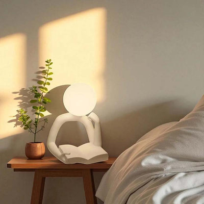 Thinker Statue LED Table Lamp sits on a wooden nightstand next to a small potted plant.