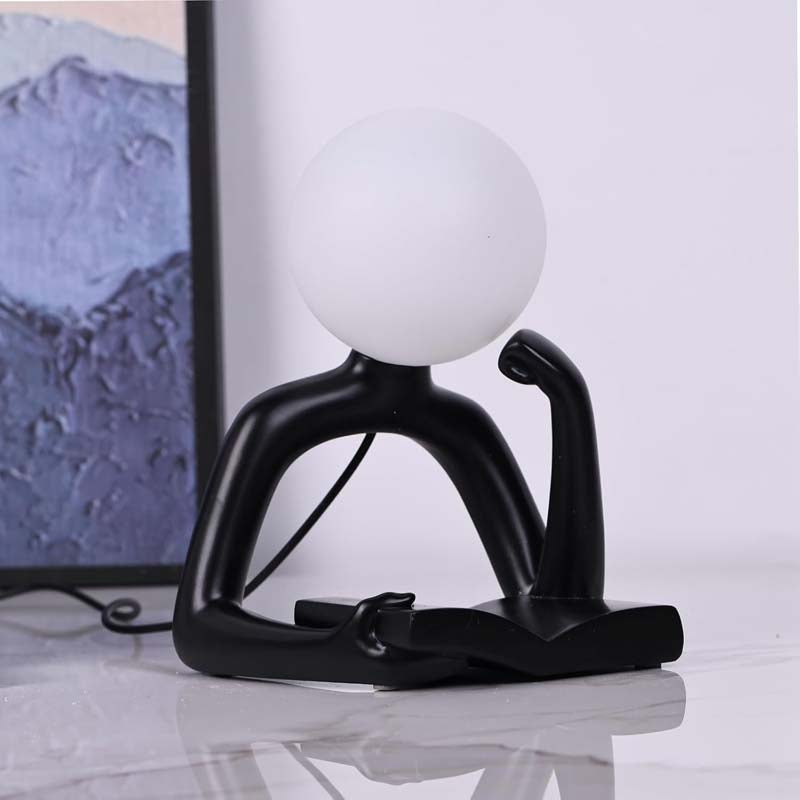 The Thinker Statue LED Table Lamp stands on a glossy white surface against a blurred interior background.