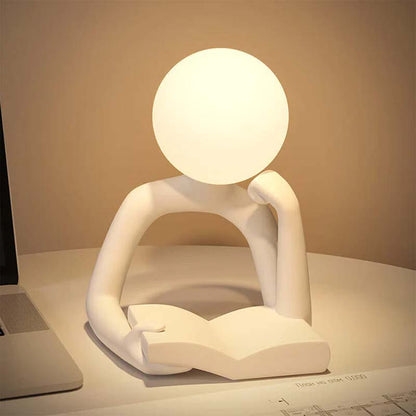Thinker Statue LED Table Lamp sits on a tabletop next to a laptop.