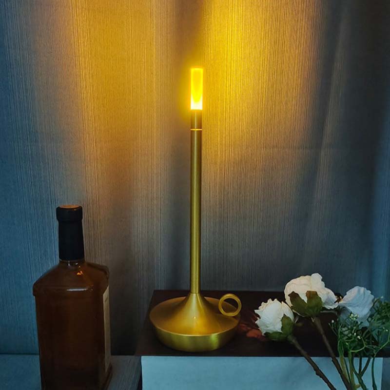 Gold lamp on a table with a bottle and flowers against a textured wall.